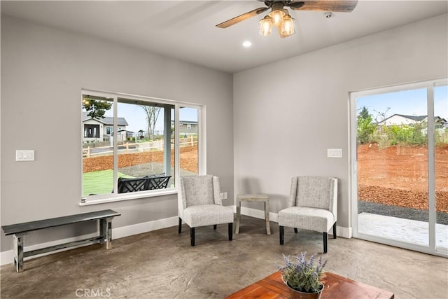 living area with ceiling fan, baseboards, concrete flooring, and plenty of natural light