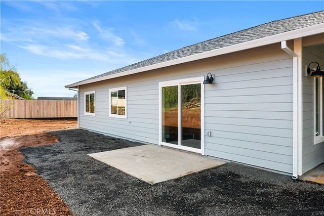 back of property with a patio area, a shingled roof, and fence