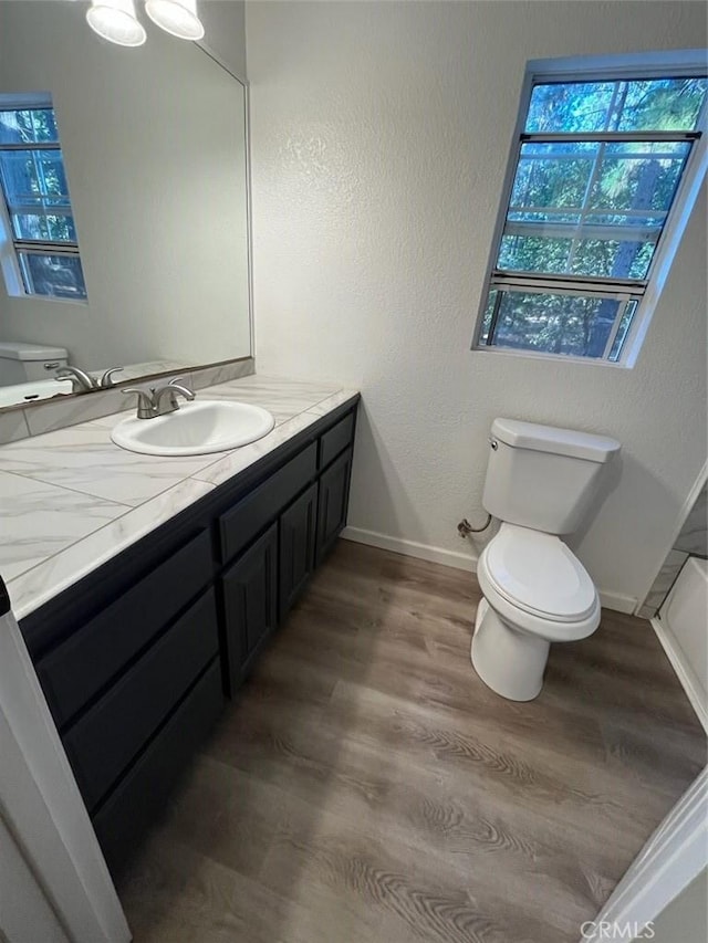 bathroom with baseboards, wood finished floors, vanity, and toilet