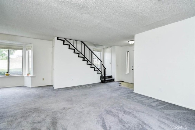 unfurnished living room with a wealth of natural light, stairway, carpet, and baseboards