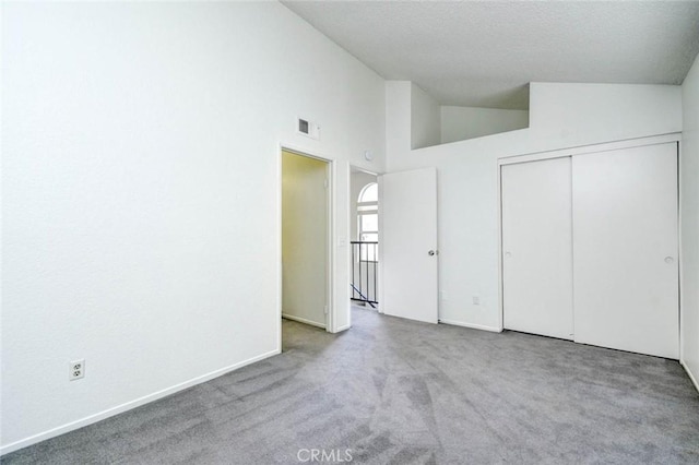 unfurnished bedroom featuring a closet, a textured ceiling, visible vents, high vaulted ceiling, and carpet