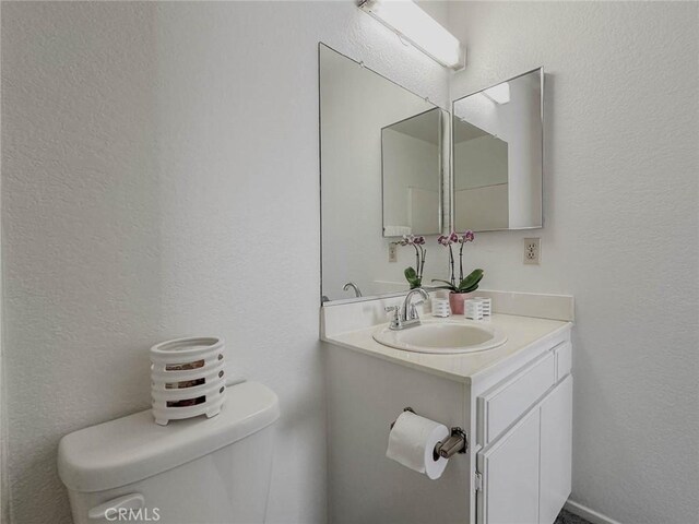 half bath with a textured wall, vanity, and toilet