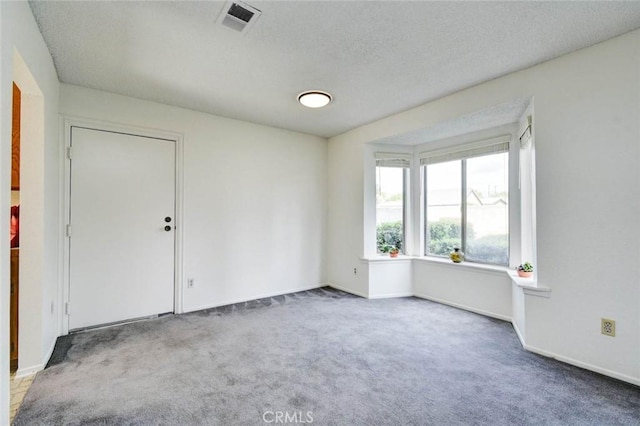 carpeted spare room with visible vents, baseboards, and a textured ceiling