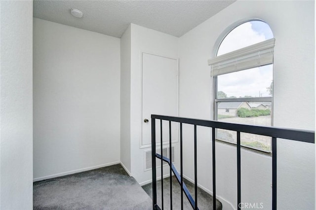 hall with a textured ceiling, visible vents, carpet flooring, an upstairs landing, and baseboards