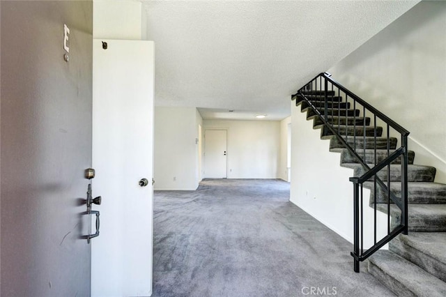 stairway with a textured ceiling, carpet flooring, and baseboards