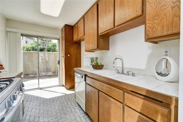 kitchen with tile countertops, white appliances, brick patterned floor, brown cabinetry, and a sink