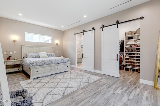 bedroom with light wood-style floors, baseboards, recessed lighting, a barn door, and a spacious closet
