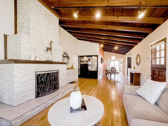 living area with vaulted ceiling with beams, wooden ceiling, wood finished floors, and a fireplace
