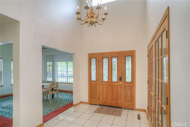 entryway featuring a chandelier, a towering ceiling, baseboards, and light tile patterned floors