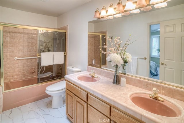 full bath featuring toilet, double vanity, a sink, and bath / shower combo with glass door