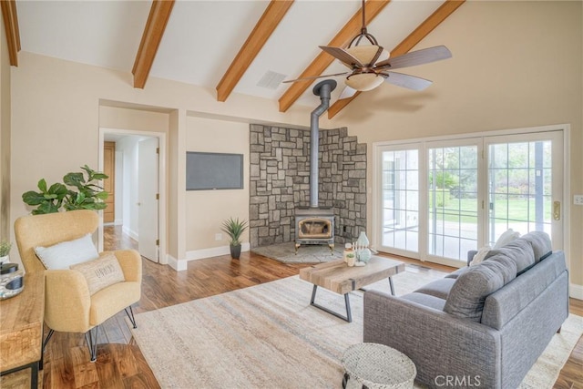 living area with a ceiling fan, beamed ceiling, a wood stove, and wood finished floors