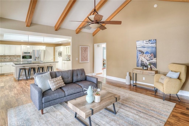 living room featuring light wood-style floors, a ceiling fan, beamed ceiling, and high vaulted ceiling