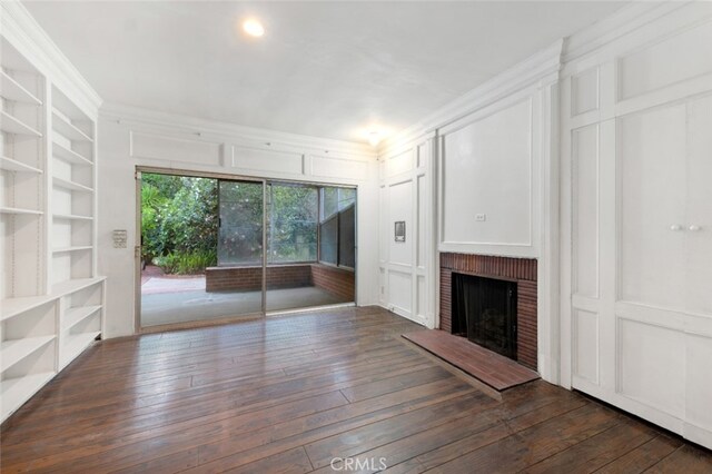 unfurnished living room featuring a decorative wall, built in shelves, hardwood / wood-style floors, and a brick fireplace