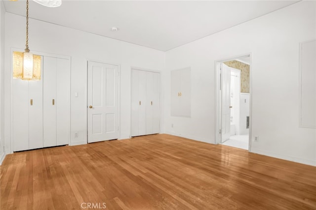 unfurnished bedroom with ensuite bathroom, multiple closets, and wood finished floors