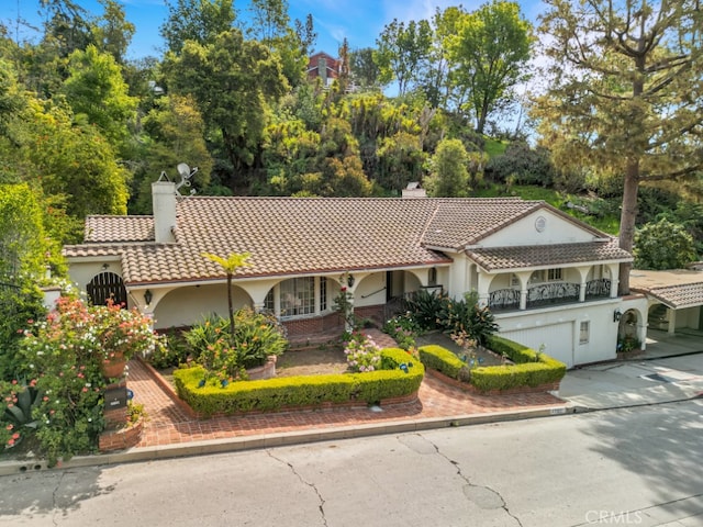 view of front facade with a balcony, stucco siding, a chimney, driveway, and a tile roof