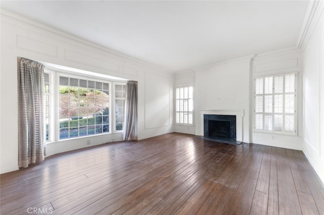 unfurnished living room with a decorative wall, ornamental molding, dark wood finished floors, and a healthy amount of sunlight