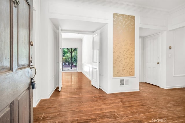 entrance foyer featuring crown molding, a decorative wall, visible vents, a wainscoted wall, and wood finished floors