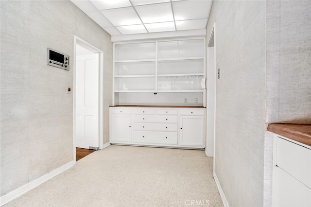 corridor featuring a paneled ceiling, light colored carpet, and baseboards