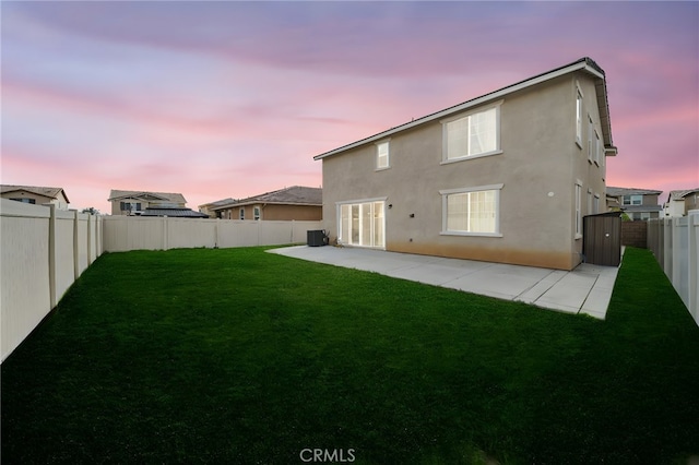 back of house at dusk with stucco siding, a lawn, a fenced backyard, central AC, and a patio area