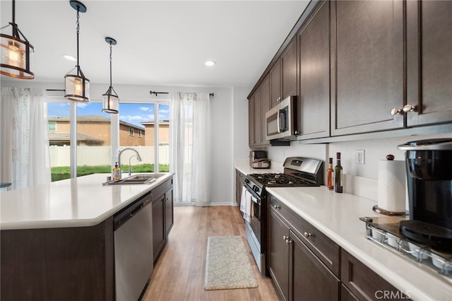 kitchen featuring light countertops, a sink, a kitchen island with sink, dark brown cabinets, and appliances with stainless steel finishes