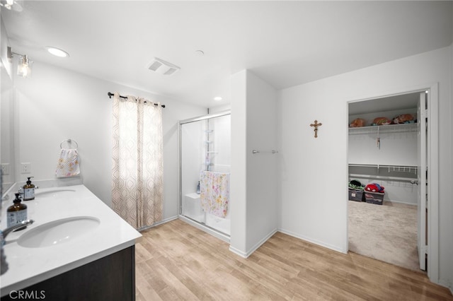 full bath featuring a shower stall, a sink, visible vents, double vanity, and wood finished floors