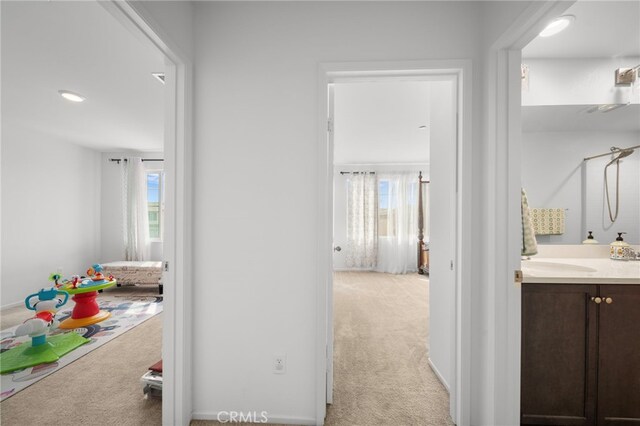 hallway featuring a sink, a healthy amount of sunlight, and light colored carpet