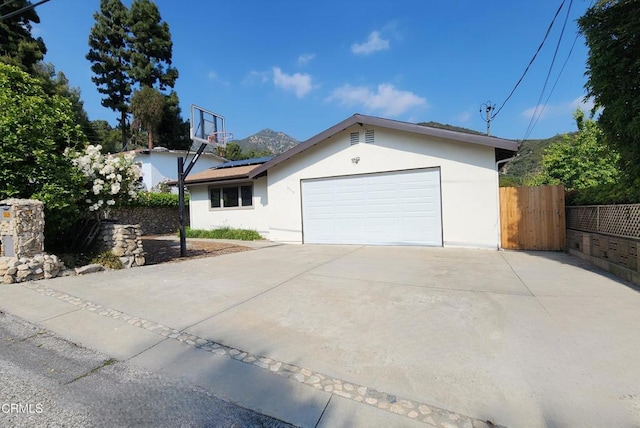view of front facade featuring fence, stucco siding, an attached garage, driveway, and solar panels