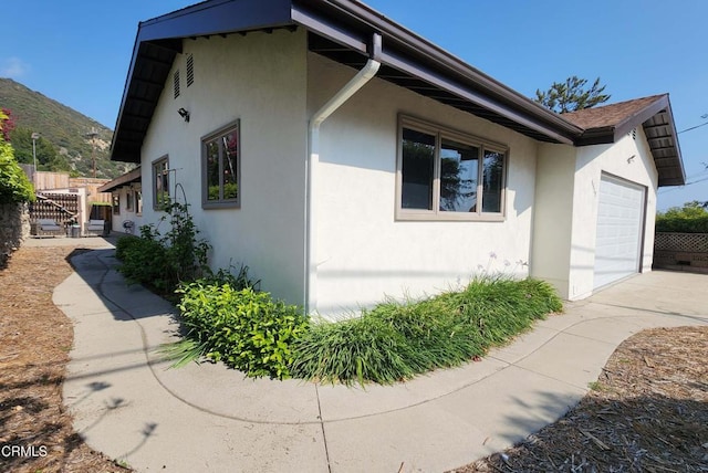 view of home's exterior featuring a garage, stucco siding, fence, and concrete driveway