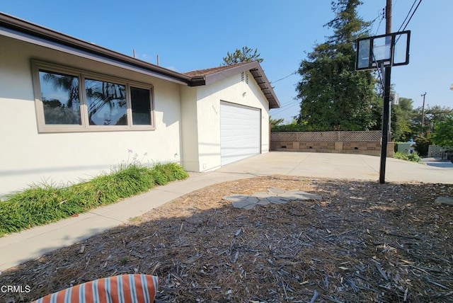 view of side of home with concrete driveway, an attached garage, fence, and stucco siding