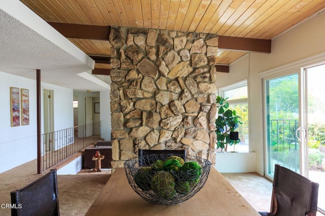 carpeted dining room with beam ceiling, a stone fireplace, and wood ceiling