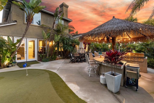 6497 Wayfinders Ct, Carlsbad, CA 92011 - patio terrace at dusk with a putting green, a patio, outdoor dining area, and an outdoor kitchen