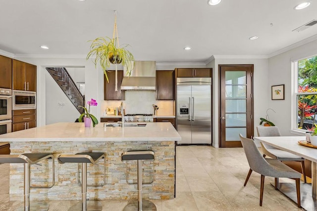6497 Wayfinders Ct, Carlsbad, CA 92011 - kitchen featuring built in appliances, wall chimney range hood, recessed lighting, a breakfast bar area, and ornamental molding