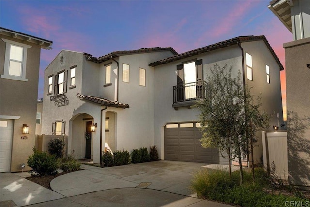 mediterranean / spanish home featuring an attached garage, driveway, a balcony, and stucco siding