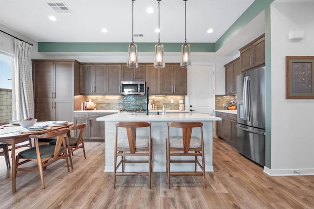 kitchen with light wood finished floors, stainless steel appliances, visible vents, and light countertops