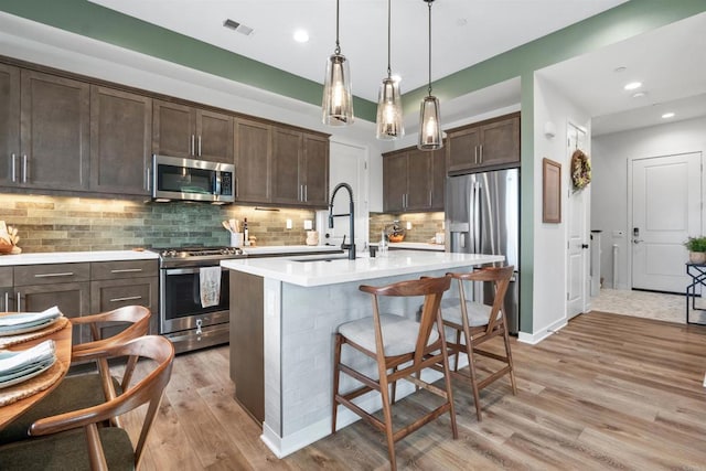 kitchen featuring stainless steel appliances, light countertops, dark brown cabinets, visible vents, and light wood-type flooring