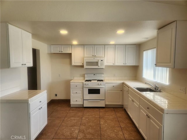 kitchen with a sink, tile countertops, white appliances, white cabinets, and baseboards
