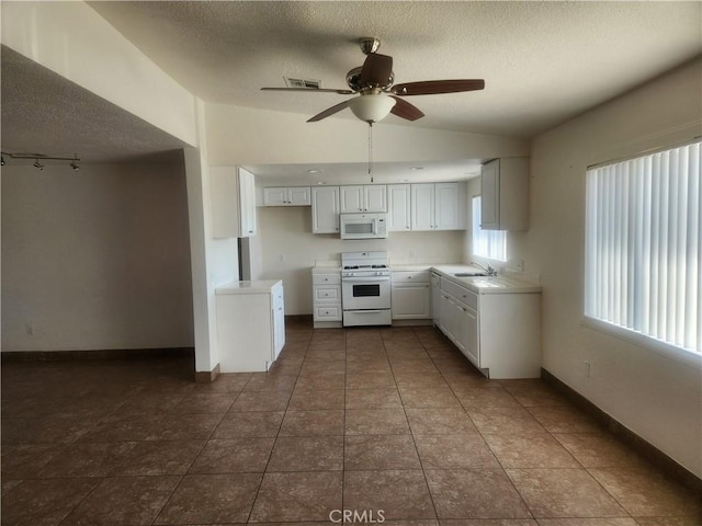 kitchen with a sink, a textured ceiling, lofted ceiling, white appliances, and ceiling fan