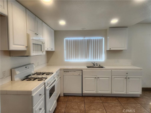 kitchen with a sink, tile countertops, white appliances, white cabinets, and tile patterned flooring