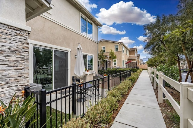 view of property exterior featuring central AC unit, stucco siding, fence, and stone siding