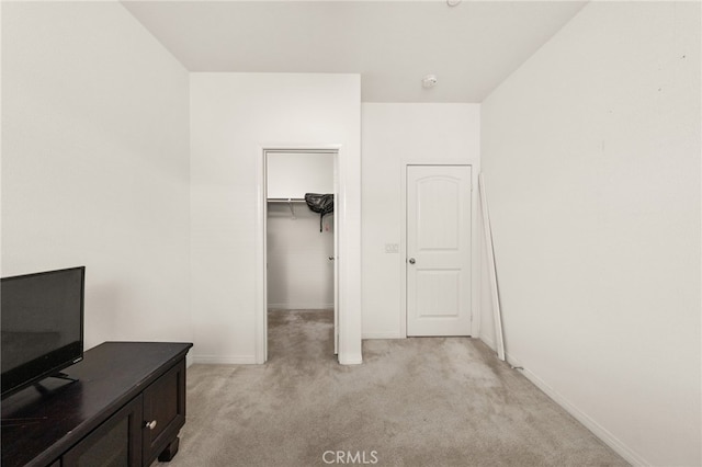 bedroom with a closet, a walk in closet, baseboards, and light colored carpet