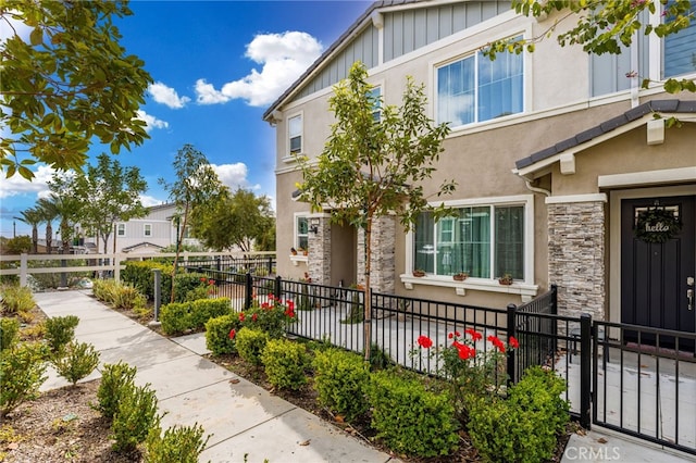 view of front of house featuring stucco siding, a fenced front yard, board and batten siding, and stone siding