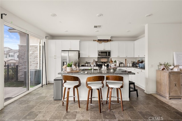 kitchen featuring white cabinetry, a kitchen bar, an island with sink, visible vents, and appliances with stainless steel finishes