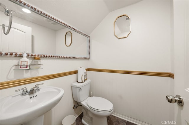 half bathroom with lofted ceiling, toilet, and a sink