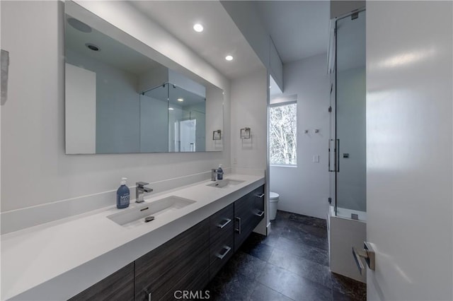 bathroom featuring toilet, double vanity, a sink, and a shower stall