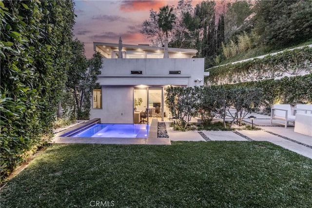 rear view of property featuring a patio, an outdoor pool, stucco siding, and a lawn