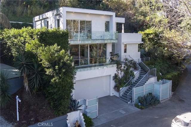exterior space featuring stucco siding, stairway, a balcony, a garage, and concrete driveway