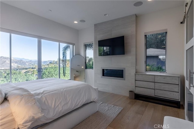 bedroom featuring wood finished floors, a mountain view, a fireplace, and recessed lighting