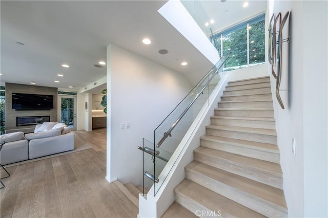 stairs with recessed lighting, a skylight, a large fireplace, and wood finished floors