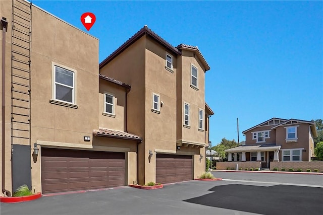 exterior space featuring a garage, a tiled roof, aphalt driveway, and stucco siding