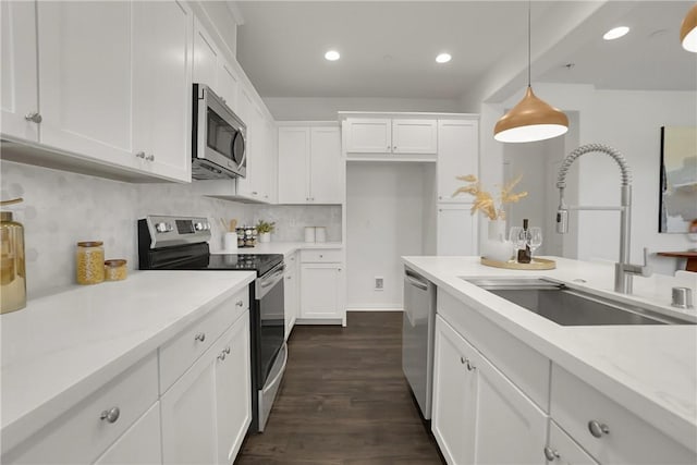 kitchen with hanging light fixtures, a sink, stainless steel appliances, white cabinetry, and dark wood-style floors